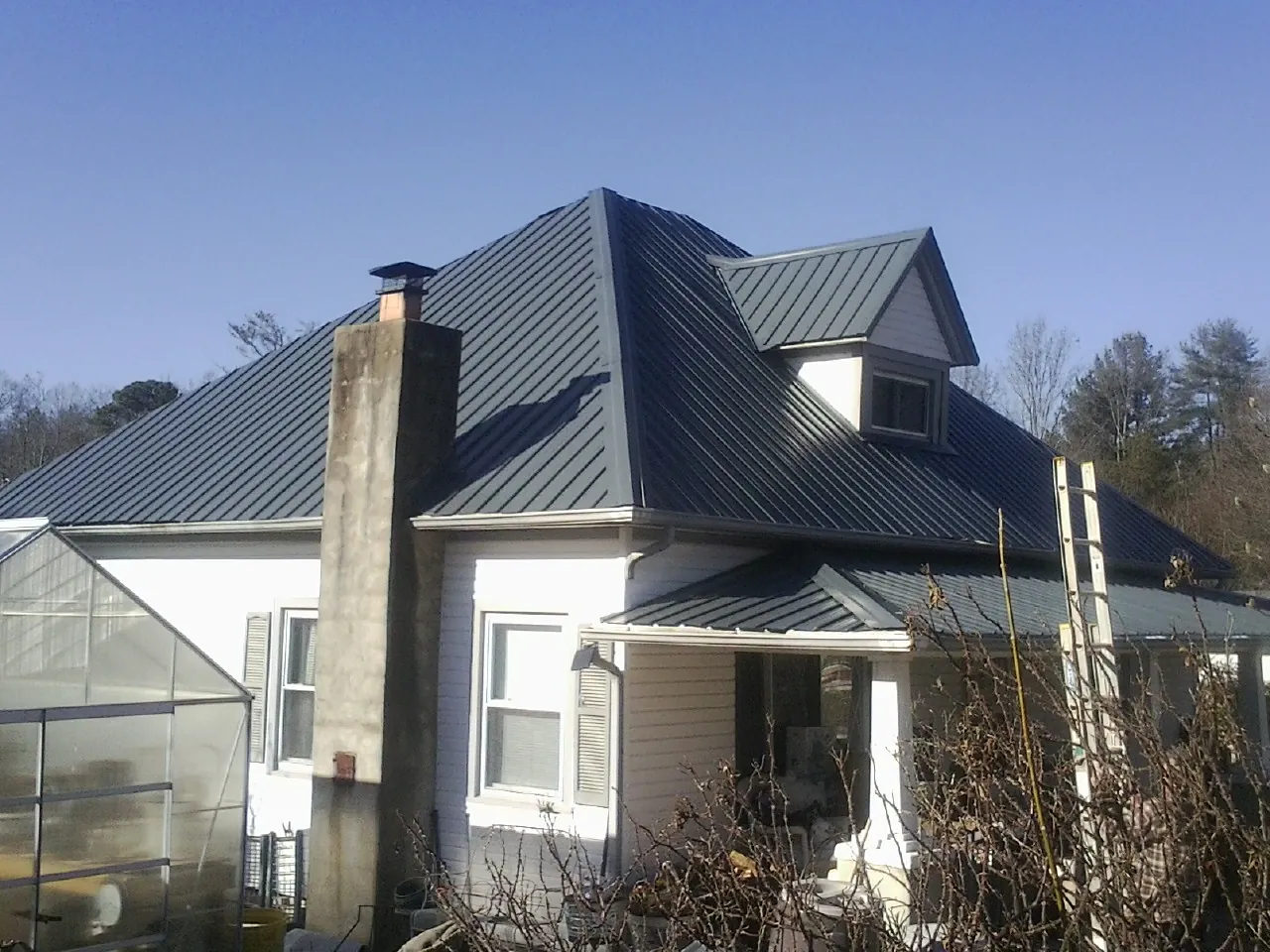 Dark blue standing seam metal roof on a white farmhouse with dormer — Slate & Tile Roof Repair by Roofing Brothers in Pipe Creek