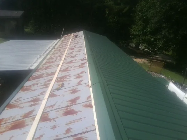 Old rusted panels beside newly installed green metal roofing — Wind Damage Roof Repair by Roofing Brothers in Pipe Creek