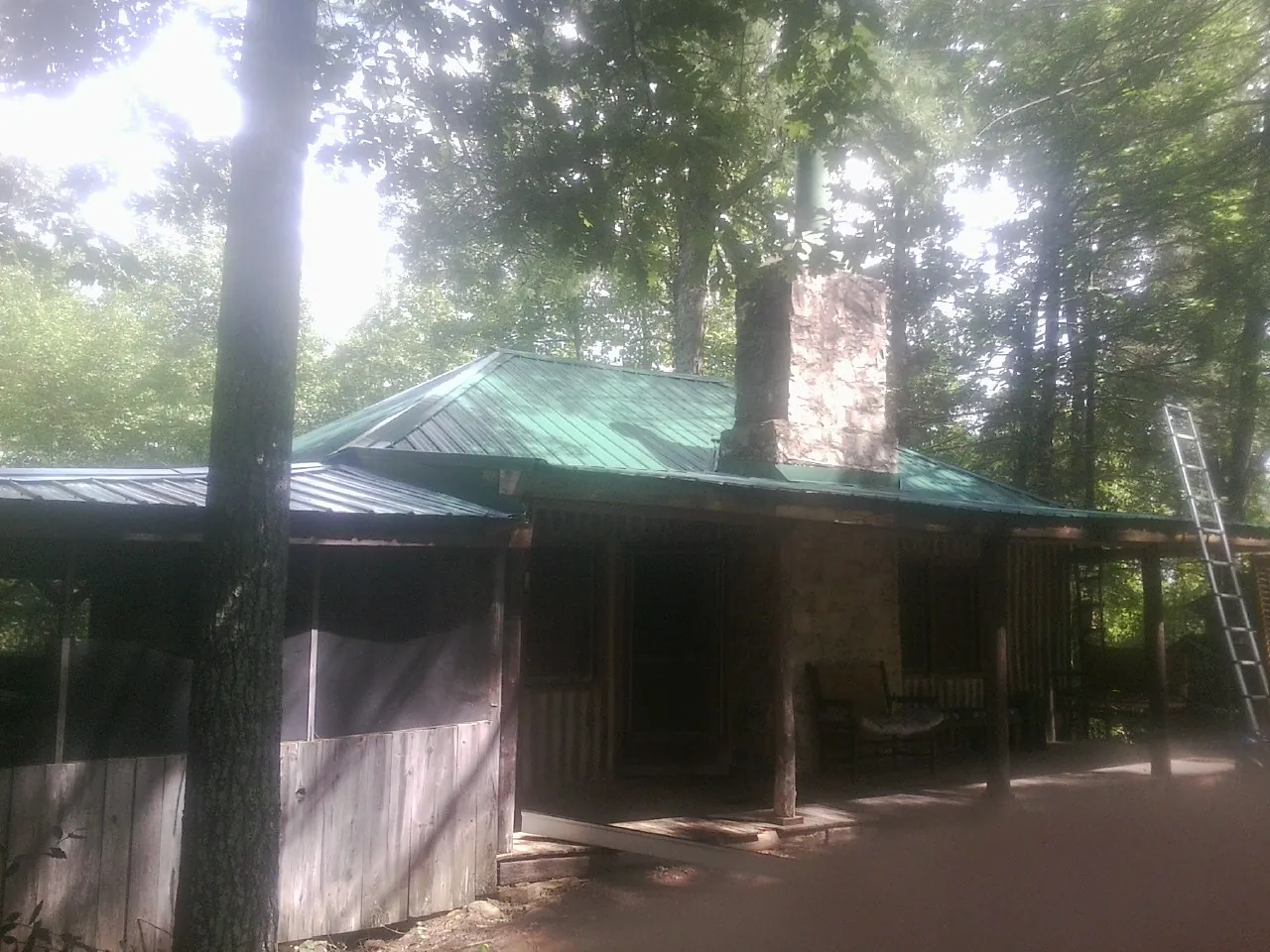 Green metal roof and stone chimney above a log cabin porch in Pipe Creek