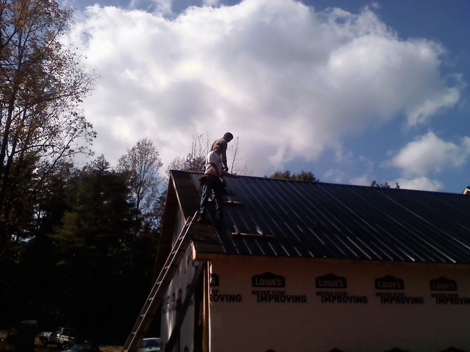 Roofer fastening dark metal panels high against a cloudy sky, from a Roof Inspection job in Pipe Creek