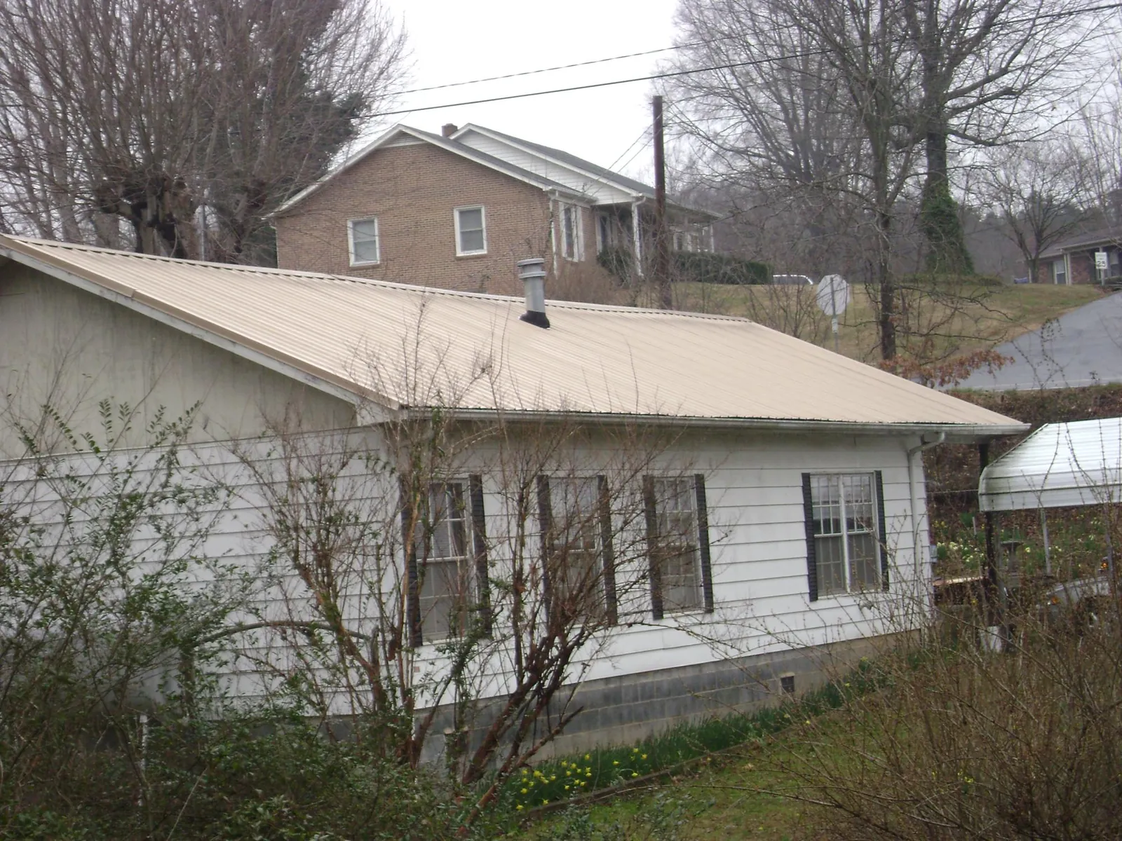 Tan metal roof on a white sided house set into a hillside — Commercial Roofing by Roofing Brothers in Pipe Creek